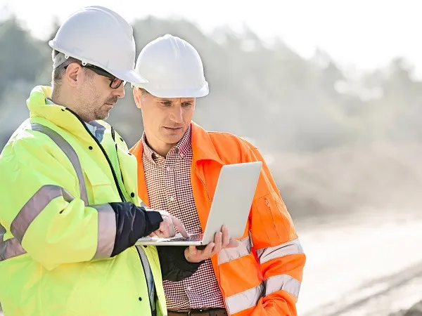 Zwei Bauleiter prüfen gemeinsam Unterlagen am Laptop auf der Baustelle